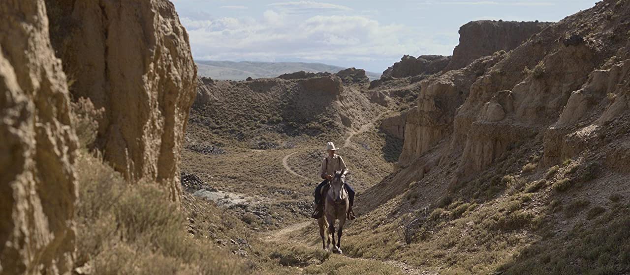 A cowboy wearing chaps rides through a valley